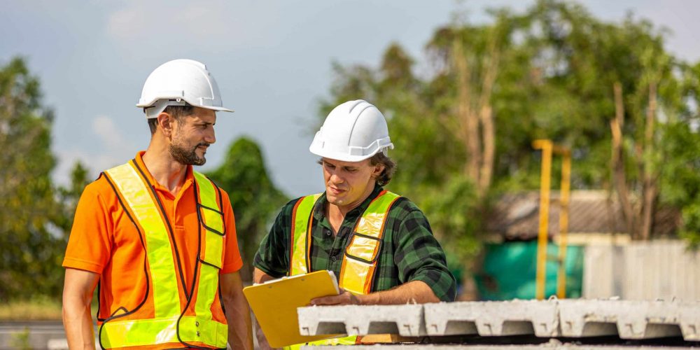 Zwei Bauarbeiter mit Schutzhelmen besprechen möglicherweise sicherheitsrelevante Aspekte gemäß RSA 21 und MVAS 99.
